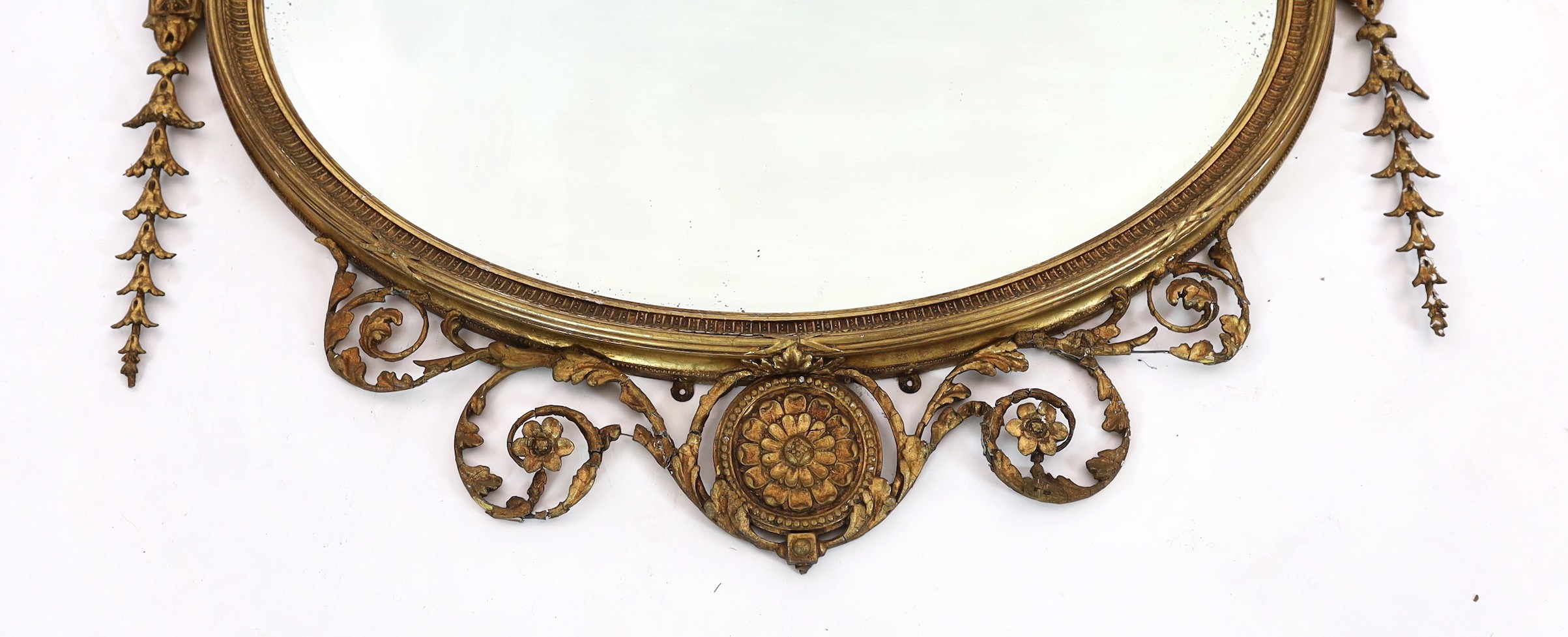 A late Victorian Adam Revival oval wall mirror, with urn, foliate scroll, ribbon and harebell motifs, and bevelled glass plate, width 119cm, height 118cm